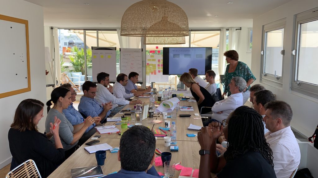 Une équipe élargie réunie autour d'une même table Une quinzaine de participants assis autour d'une longue table de travail, une intervenante debout près d'un écran, configuration possible d'un programme de séminaire de deux jours